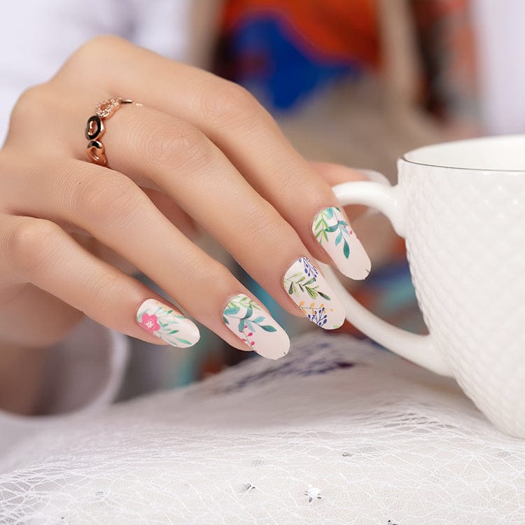Hand holding white mug displaying floral nail art wraps with delicate botanical design patterns