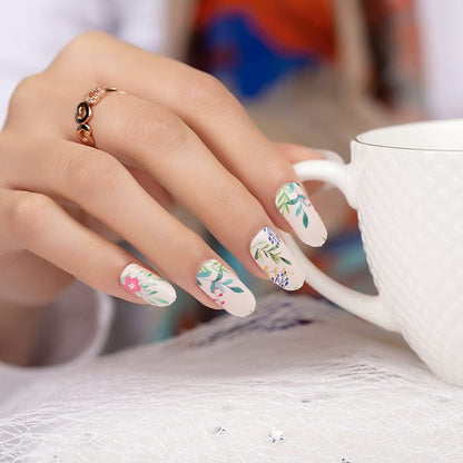Hand holding white mug displaying floral nail art wraps with delicate botanical design patterns