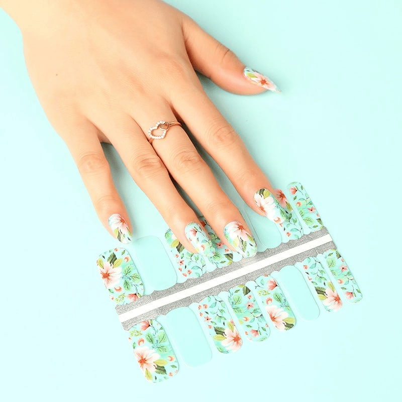 Mint green nail wraps with coral pink floral pattern shown on hand with matching nail strip sheet