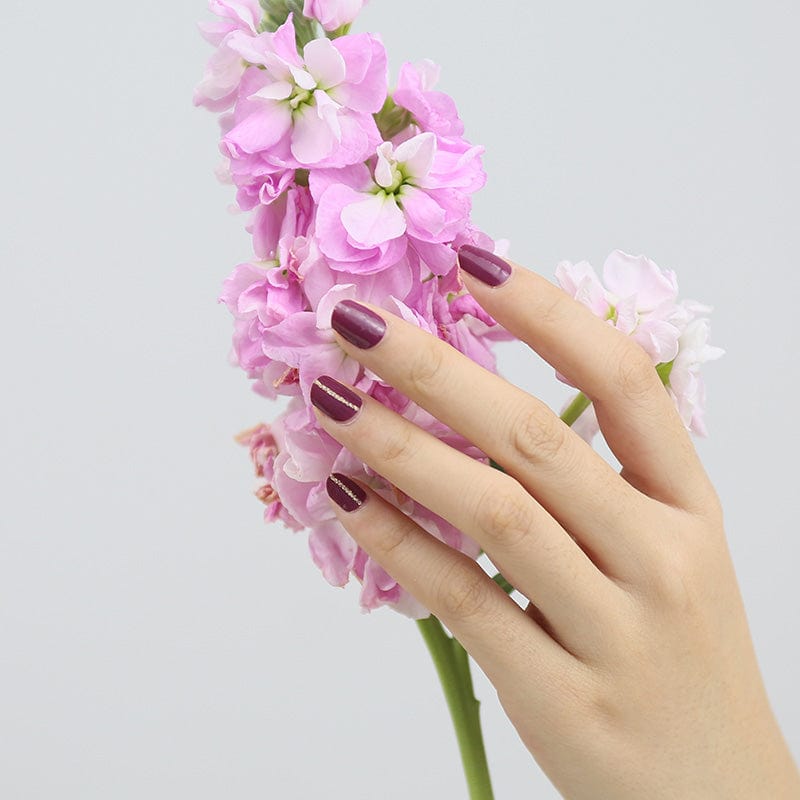 Hand with burgundy gel nail wraps holding pink flowers showing elegant wine manicure