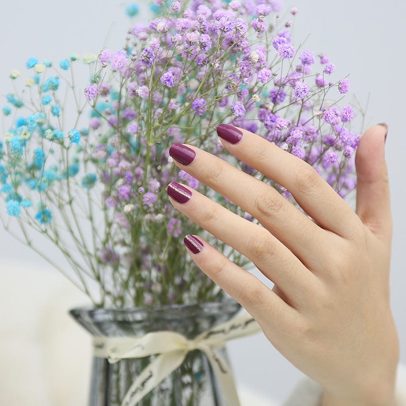 Deep burgundy nail wraps on hand with purple flowers showing glossy wine manicure