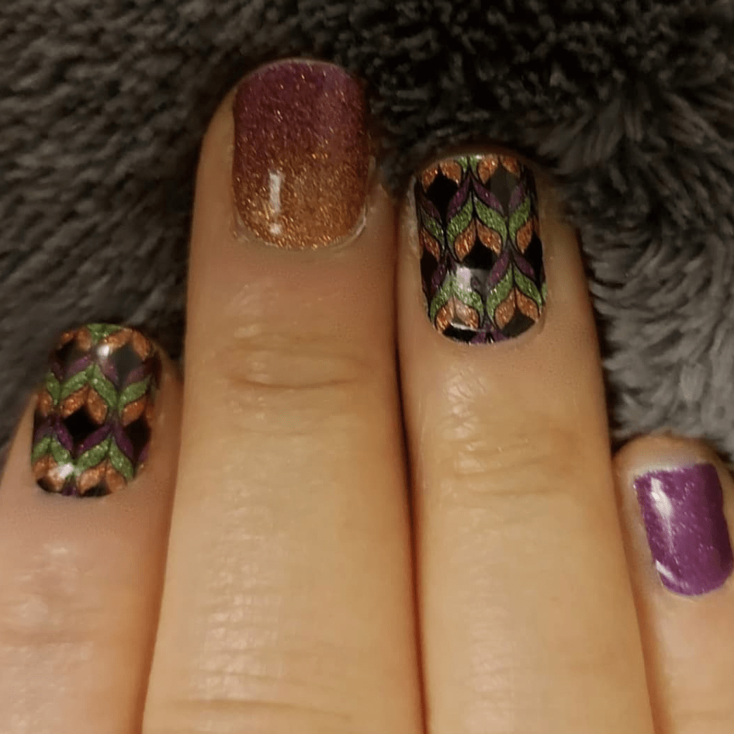 Hand wearing colourful autumn leaf pattern nail wraps with bronze glitter and purple gradient designs