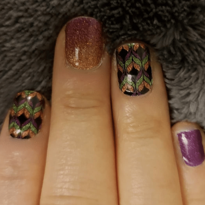 Hand wearing colourful autumn leaf pattern nail wraps with bronze glitter and purple gradient designs