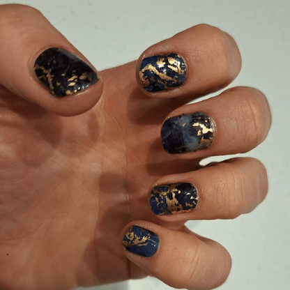 Navy blue marble nail wraps with bronze gold accents on hand showing stone pattern