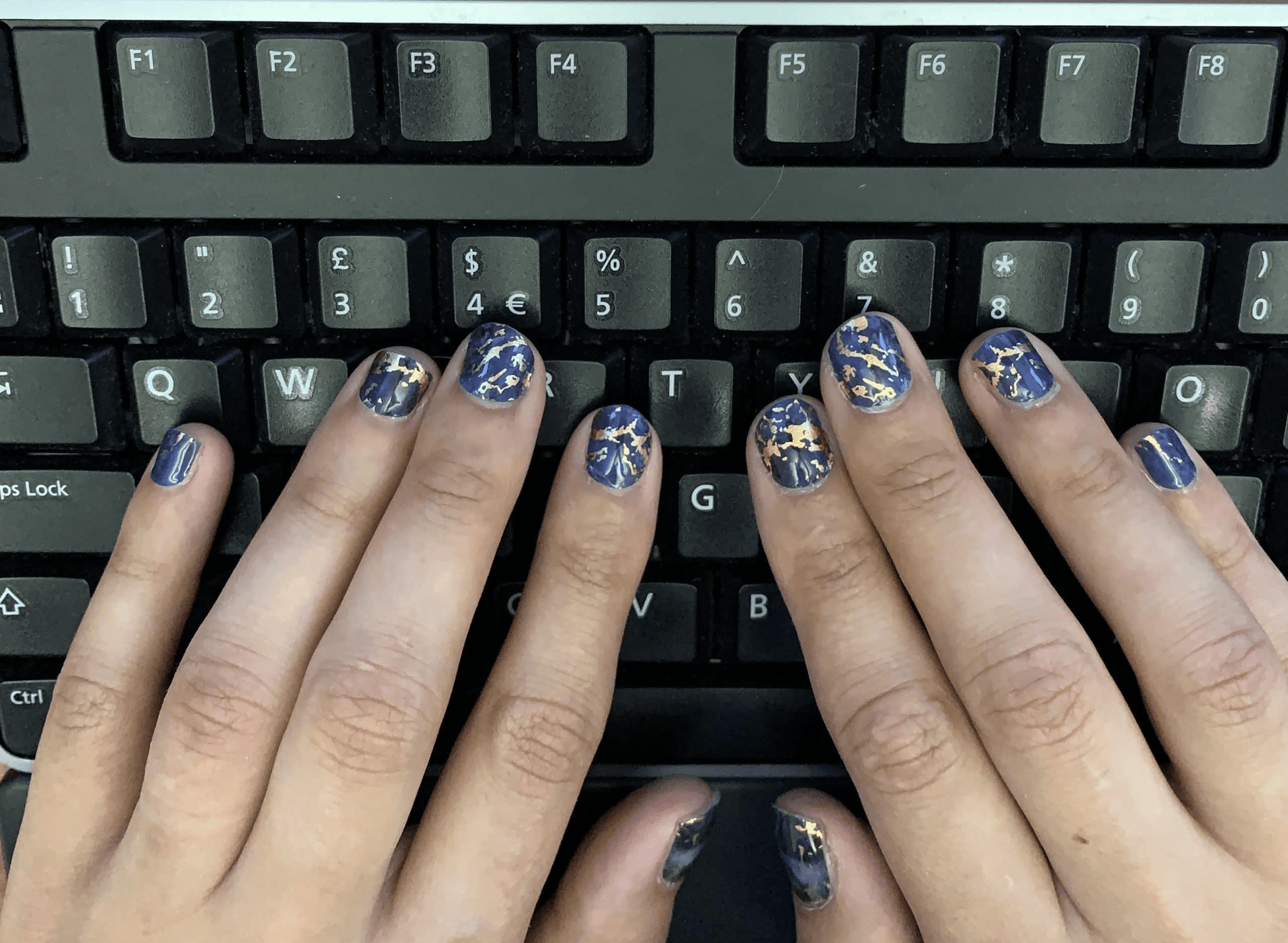 Blue marble nail wraps with gold details on hands typing on keyboard workspace