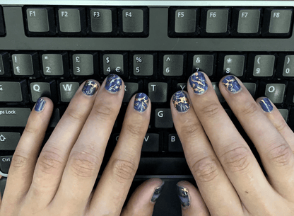 Blue marble nail wraps with gold details on hands typing on keyboard workspace