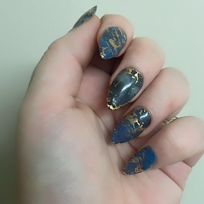 Blue marble nail wraps with gold veining on hand showing elegant stone pattern