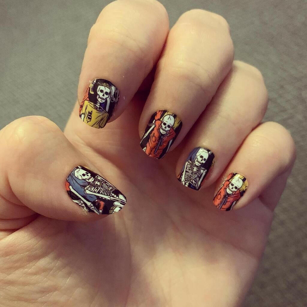 Hand wearing spooky skeleton nail wraps with colourful gothic Halloween nail art design