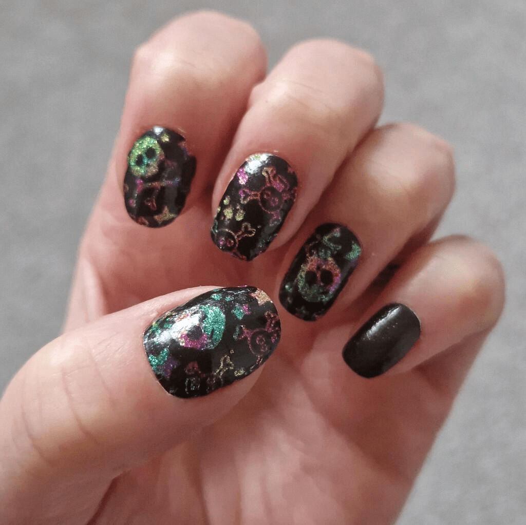 Holographic skull nail wraps on hand showing black base with rainbow glitter