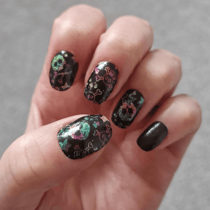 Holographic skull nail wraps on hand showing black base with rainbow glitter
