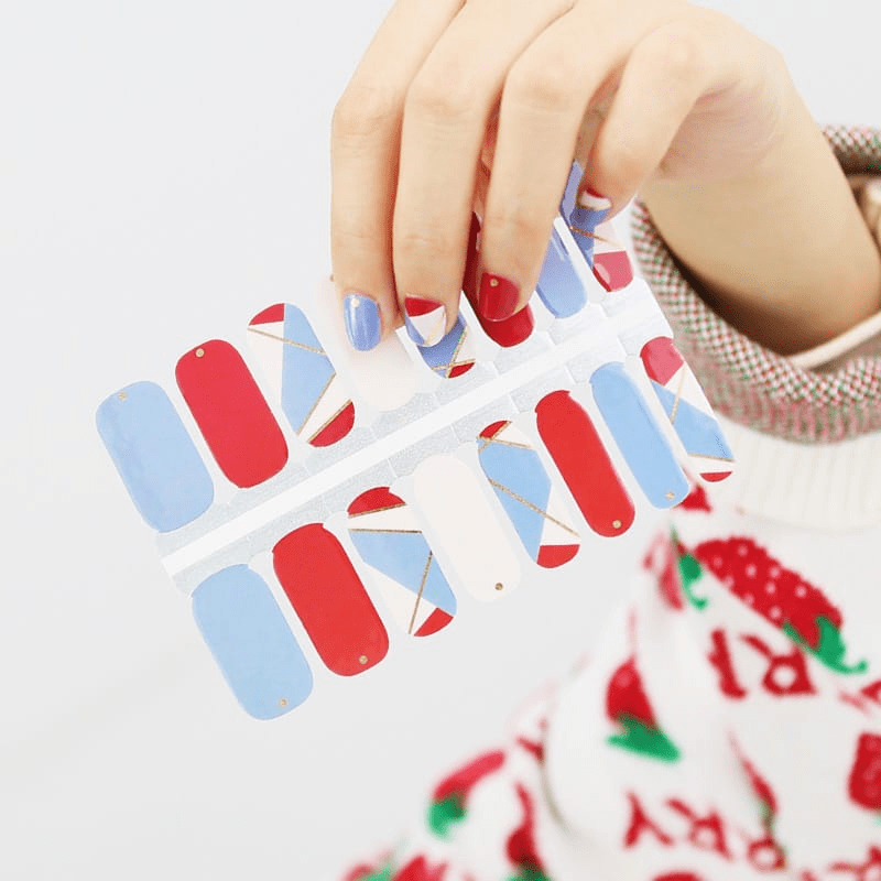 Hand holding red blue geometric nail wraps with architectural colour block patterns