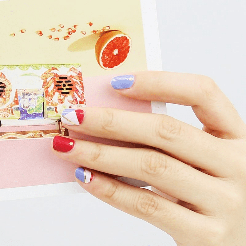 Hand wearing blue and red geometric nail wraps with gold accent stripes