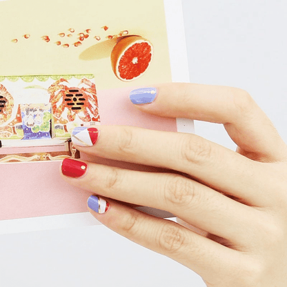 Hand wearing blue and red geometric nail wraps with gold accent stripes