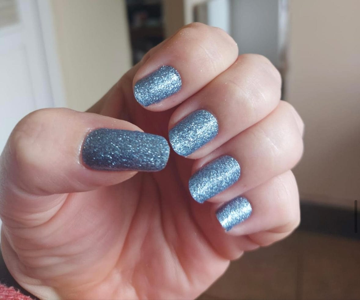 Hand displaying dusty blue glitter nail wraps with silver metallic sparkle finish