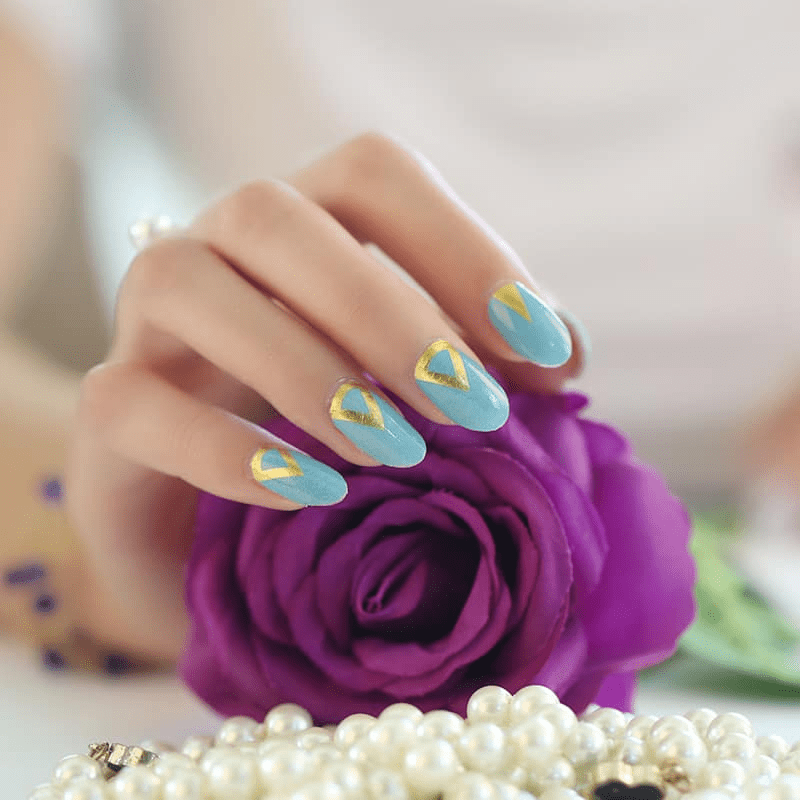 Teal nail wraps with gold triangle design on hand holding purple rose