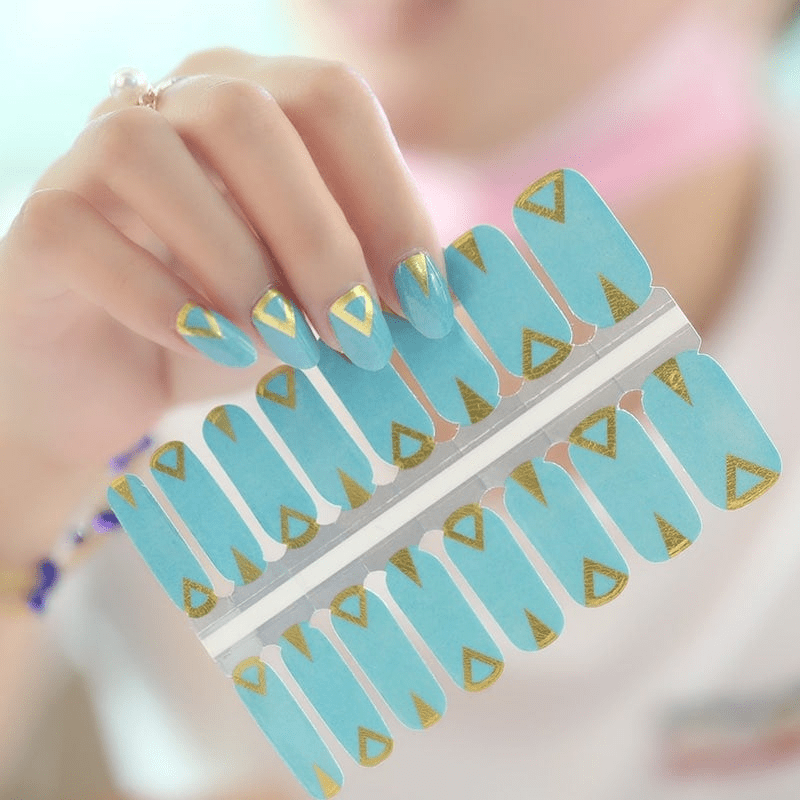 Hand displaying turquoise nail wraps with gold geometric triangular patterns
