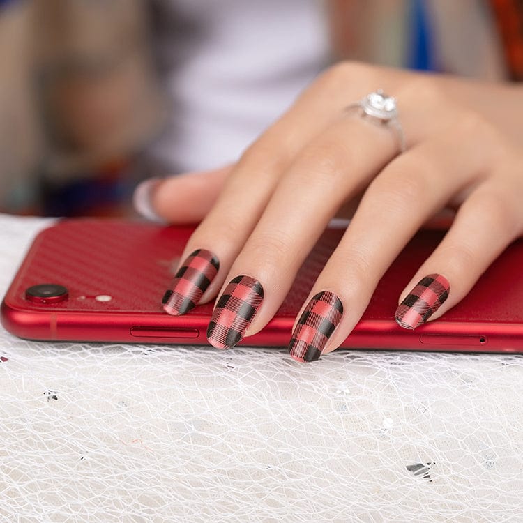 Hand with red and black buffalo check plaid nail wraps on phone