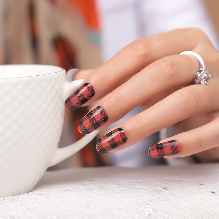 Manicured hand holding white mug showing red black plaid nail wraps