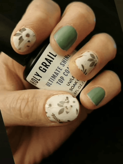 Hand wearing sage green and botanical floral nail wraps with delicate leaf patterns