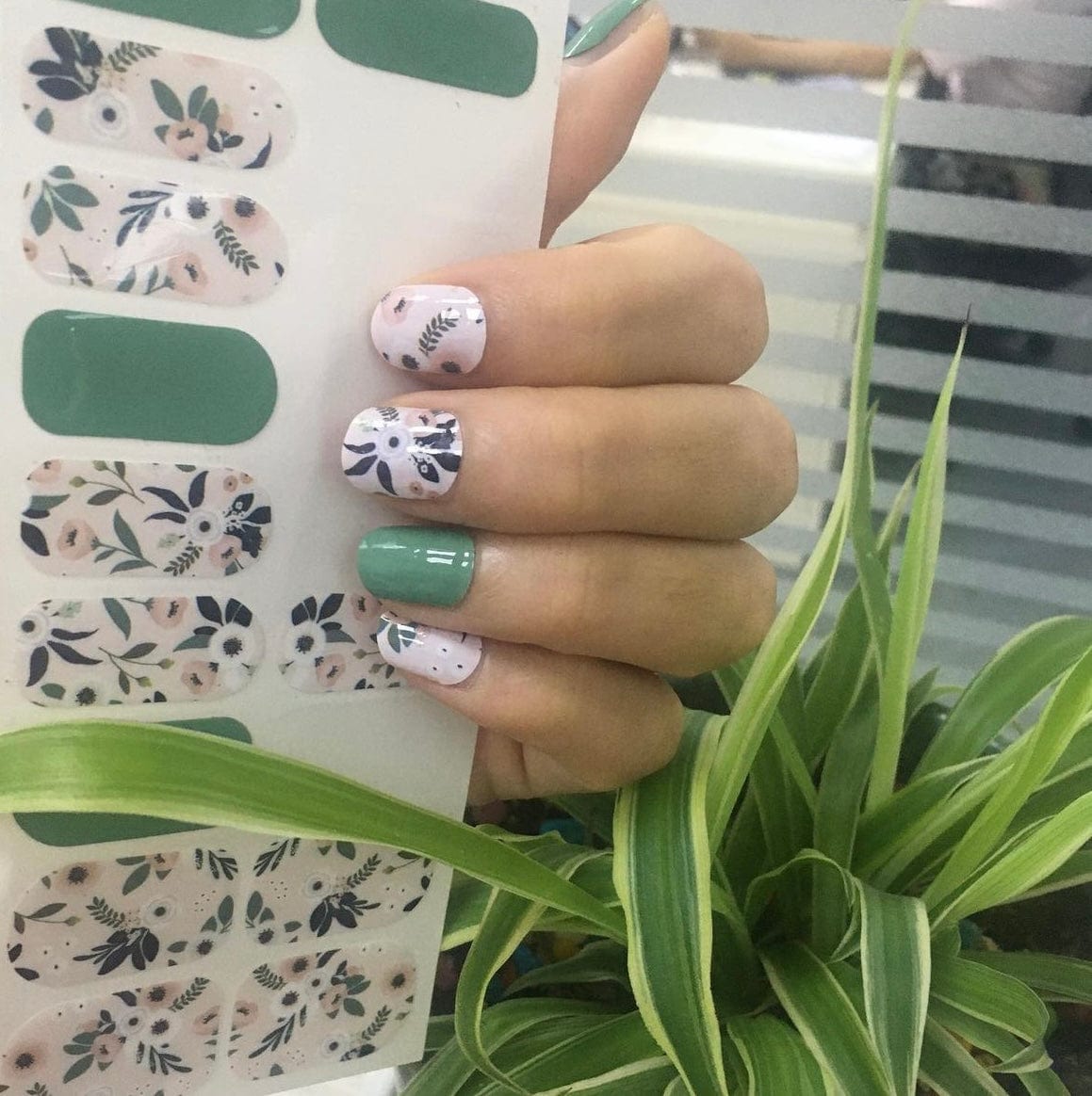 Sage green and cream botanical nail wraps with floral leaf designs on hand