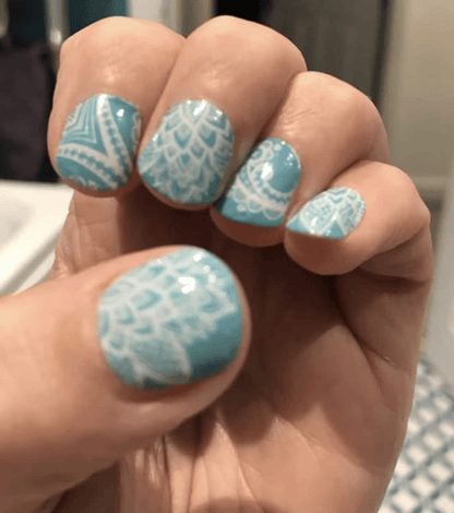 Turquoise nail wraps with white mandala patterns on hand showing boho nail art design