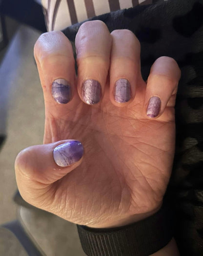 Hand wearing purple marble nail wraps displaying soft lavender watercolor stone pattern design