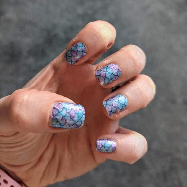Hand wearing blue purple mermaid scale gel nail wraps with shimmery finish