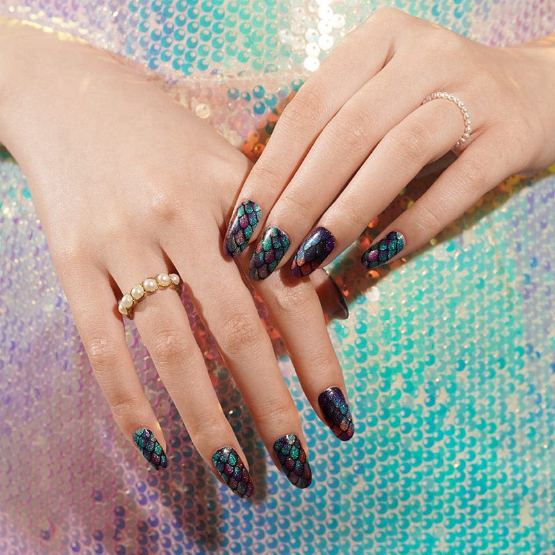 Hands with holographic mermaid scale nail wraps against sparkly sequined background