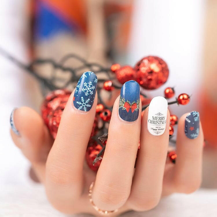Hand wearing festive Christmas nail art featuring blue snowflake patterns and red bow designs on fingers
