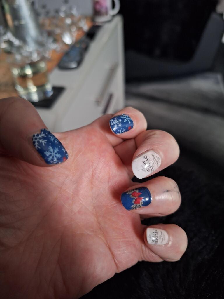 Hand displaying Christmas nail wraps in navy blue with white snowflakes and festive holiday patterns