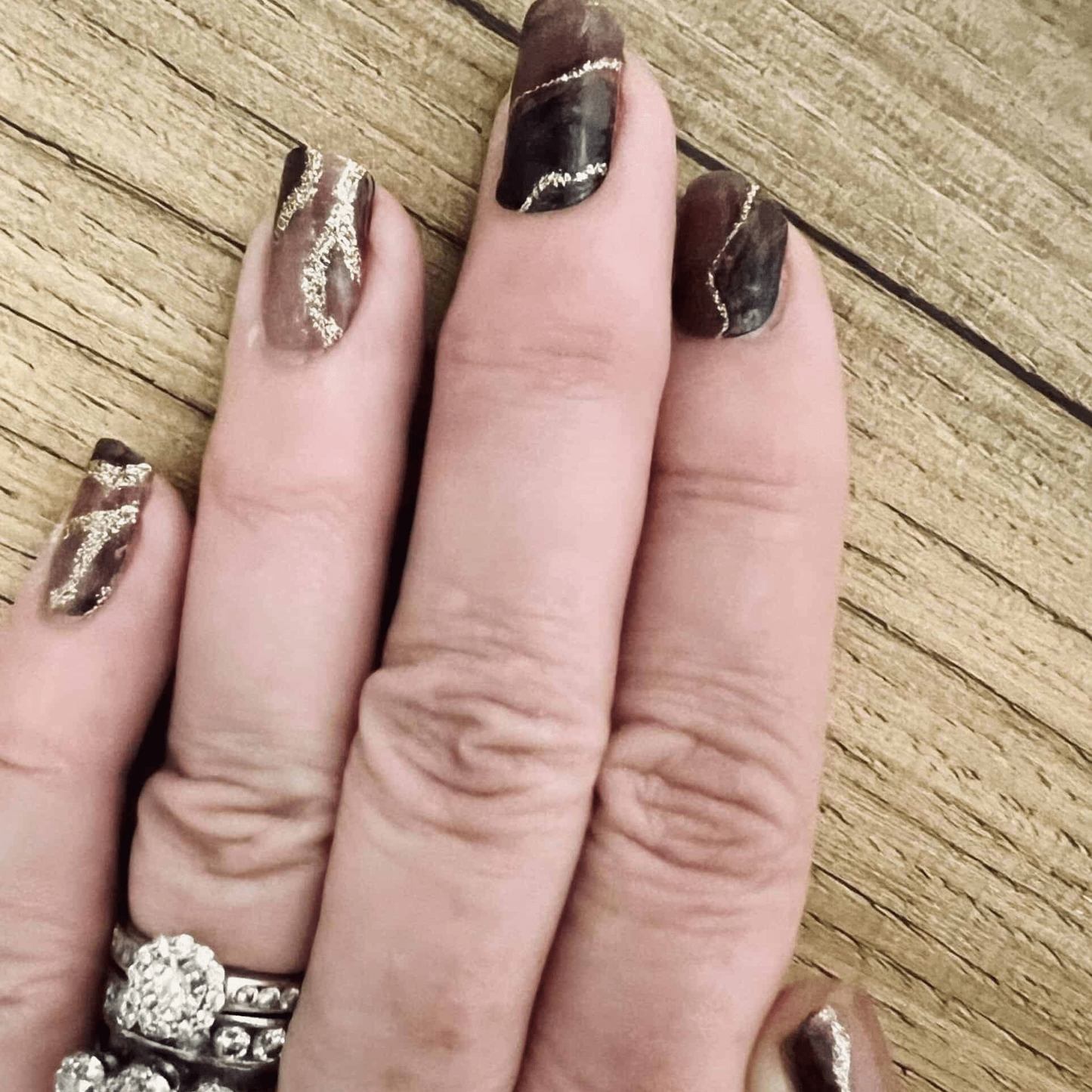 Gothic marble nail wraps with rose gold accents on hand over wooden background