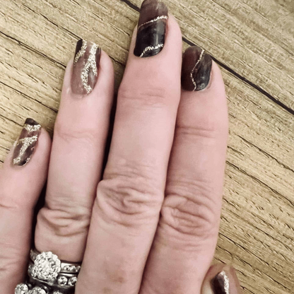 Gothic marble nail wraps with rose gold accents on hand over wooden background