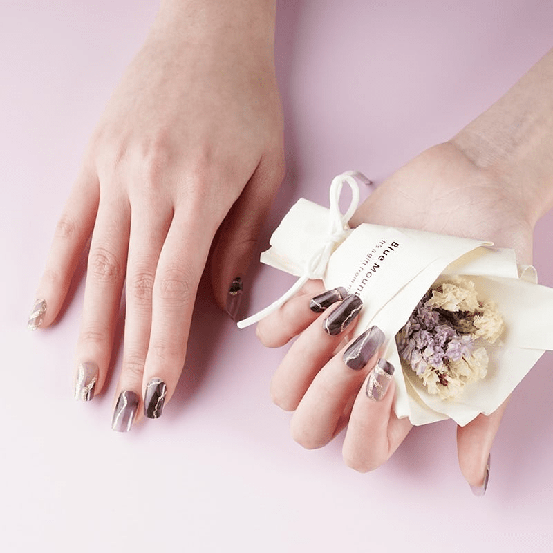 Sophisticated dark marble nail wraps with gold veining displayed with decorative flower