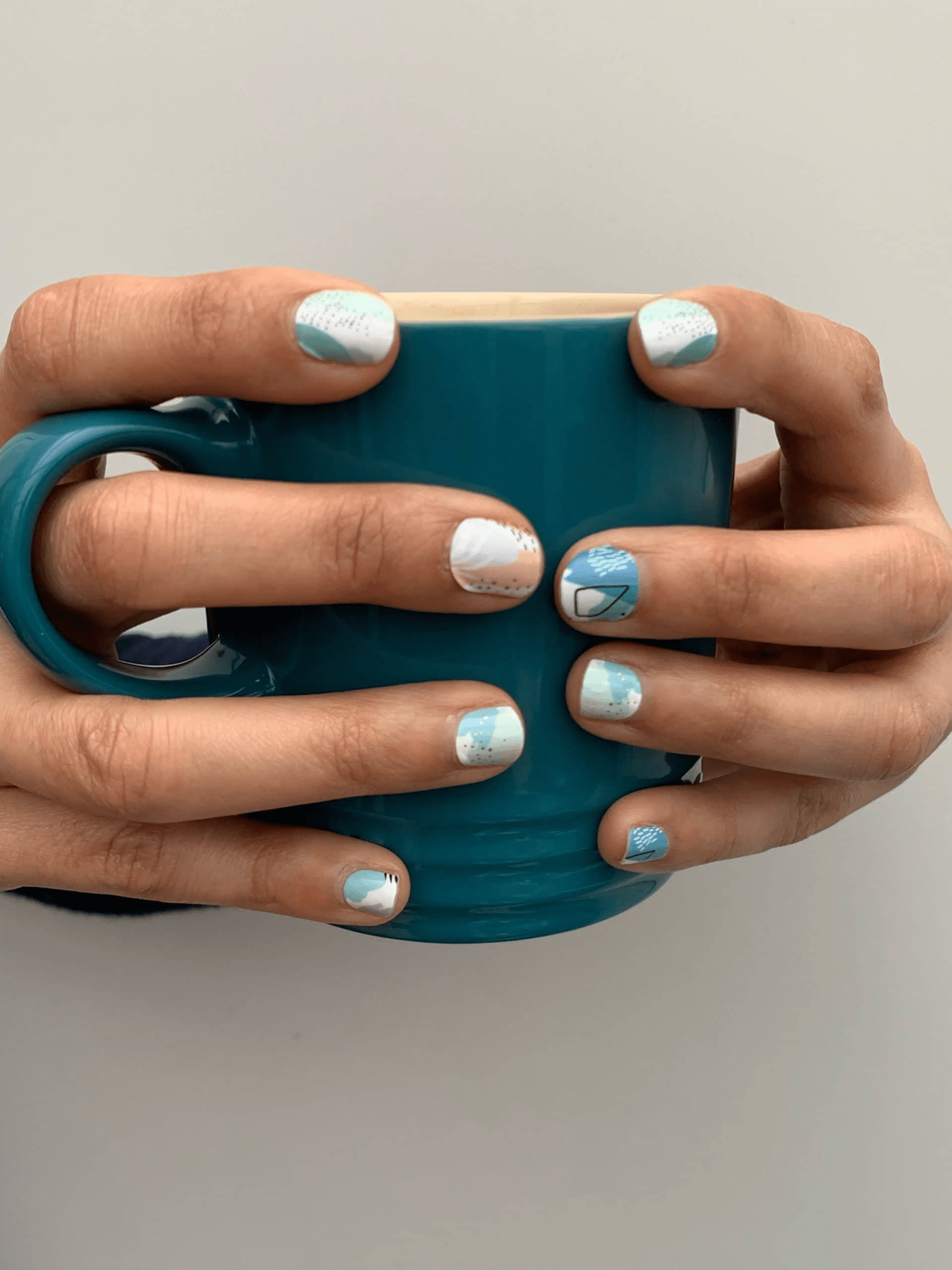 Hands holding teal mug displaying abstract watercolour nail wraps in pastel pink and mint