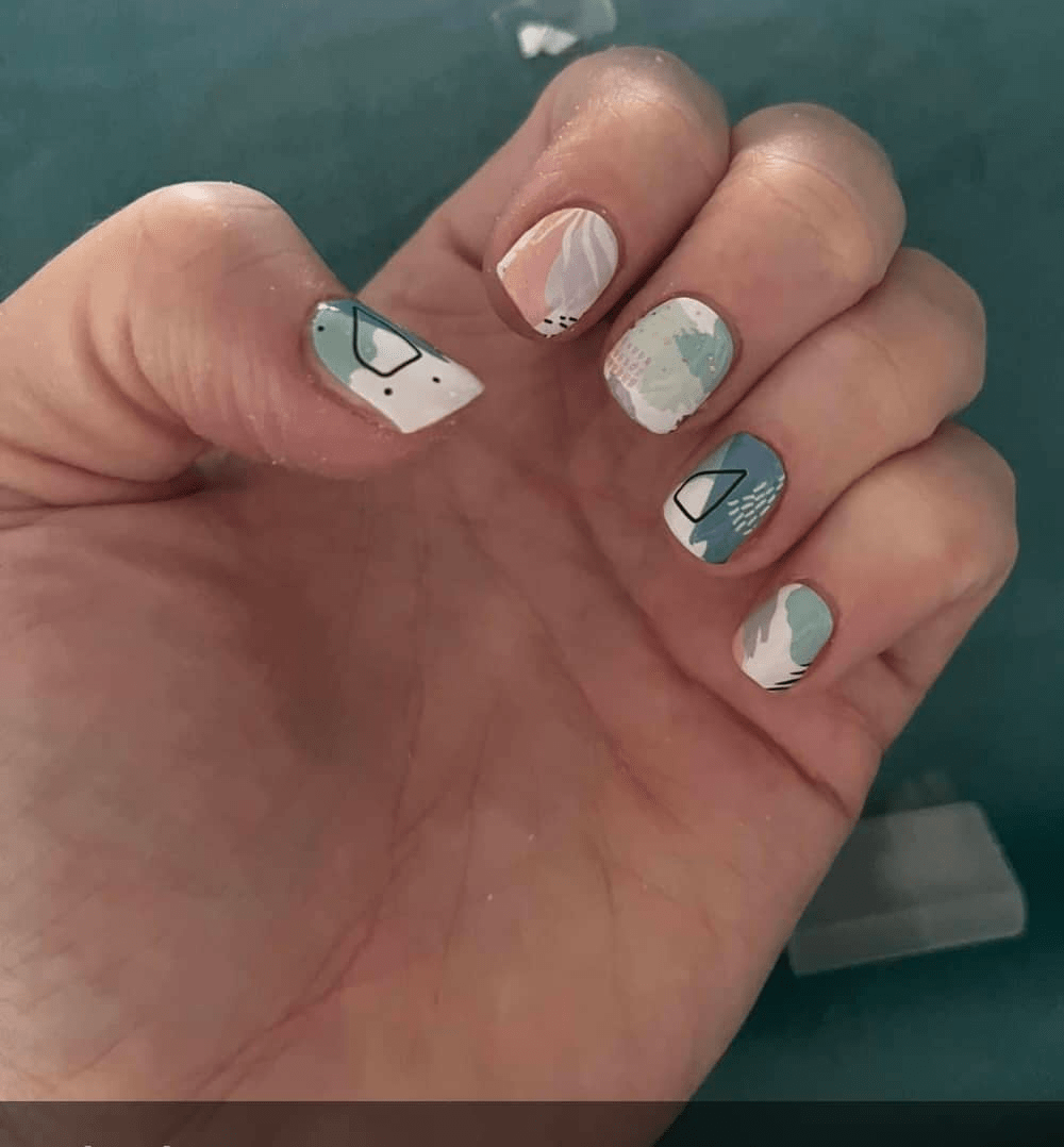 Hand wearing pastel watercolour nail wraps with abstract brushstroke patterns in sage green and peach