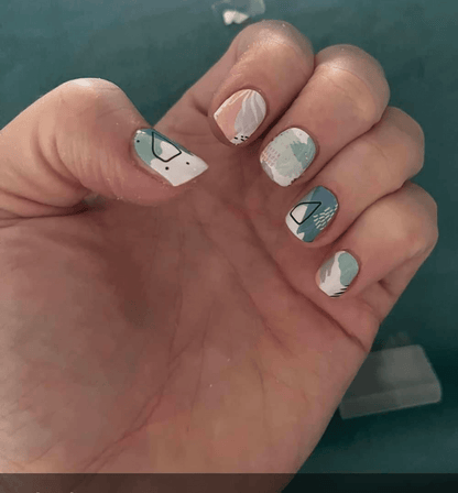 Hand wearing pastel watercolour nail wraps with abstract brushstroke patterns in sage green and peach