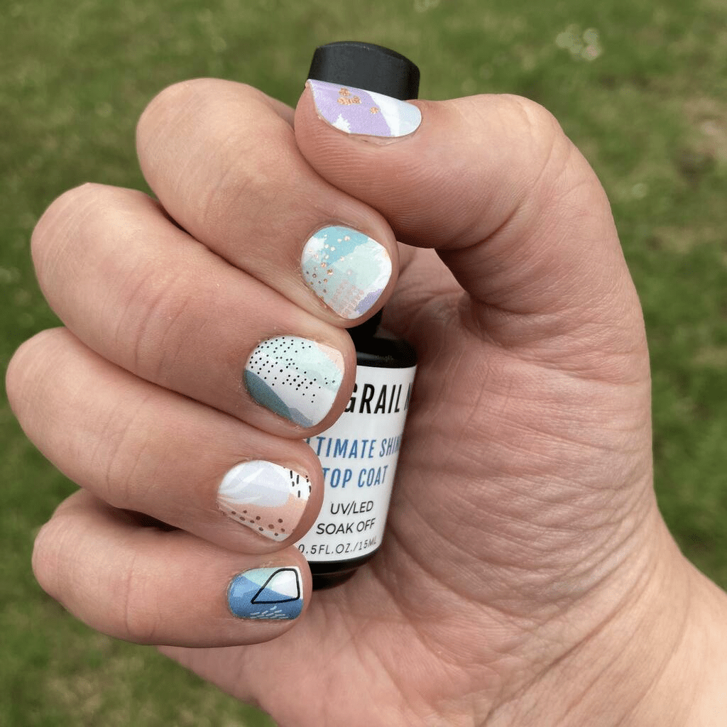 Hand holding nail care bottle showing multicolour abstract gel nail wraps with watercolour design