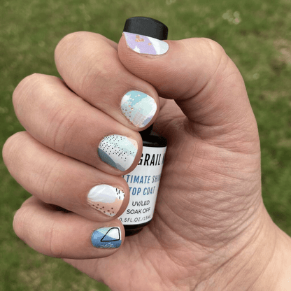 Hand holding nail care bottle showing multicolour abstract gel nail wraps with watercolour design