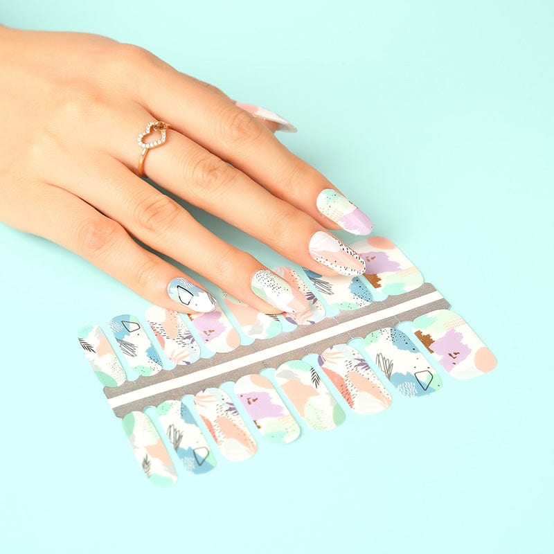 Hand holding watercolour nail wrap sheet showing abstract pastel design for DIY manicure application