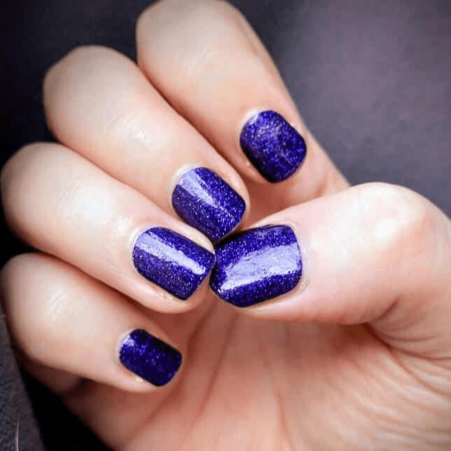 Hand displaying deep purple glitter non-UV nail wraps with sparkly finish for at-home manicure