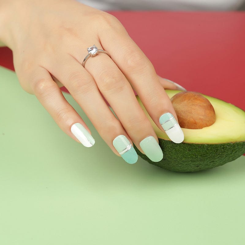 Hand with mint green striped gel nail wraps holding fresh avocado