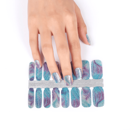 Hand applying teal holographic nail wraps with blue glitter sparkle pattern strips
