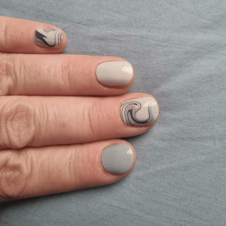 Neutral marble nail wraps on hand showing sage green and cream tones with swirl patterns