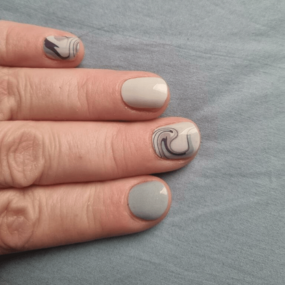 Neutral marble nail wraps on hand showing sage green and cream tones with swirl patterns