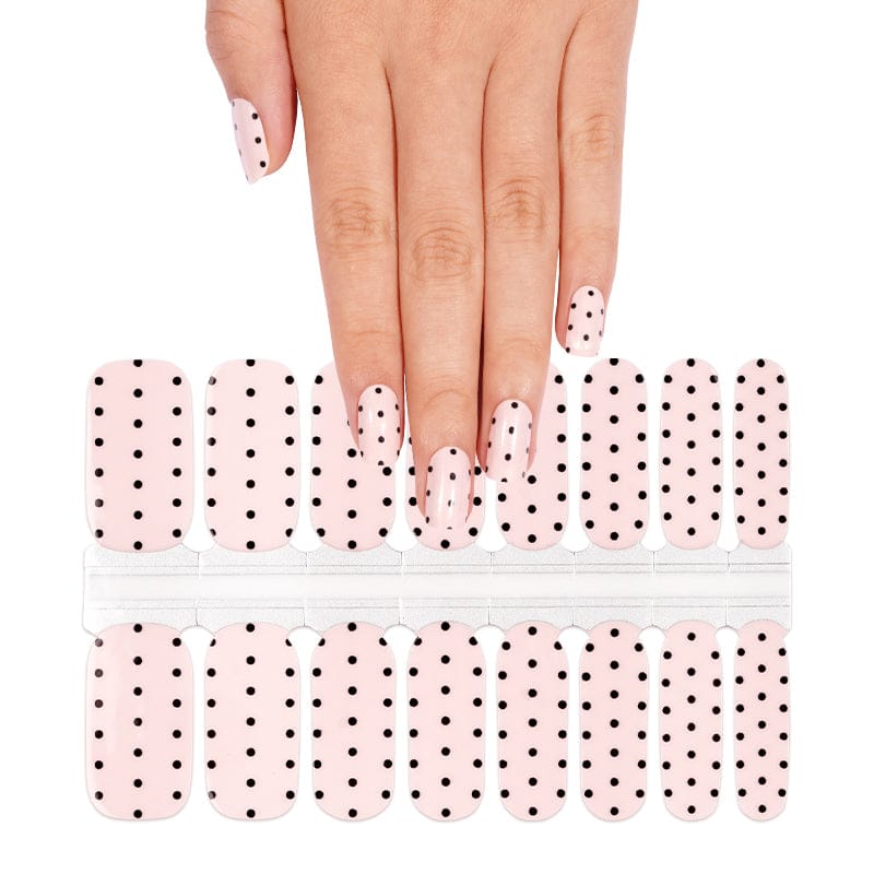 Hand wearing white polka dot nail wraps with nail wrap sheet showing classic dot pattern