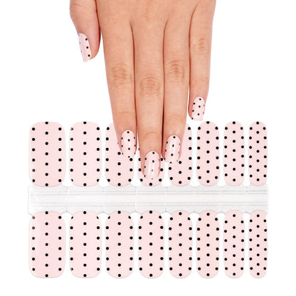 Hand wearing white polka dot nail wraps with nail wrap sheet showing classic dot pattern