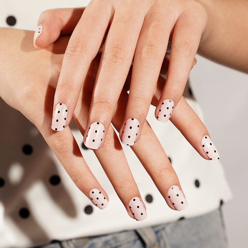 Hands showing modern black polka dot nail wraps on white base for minimalist nail art