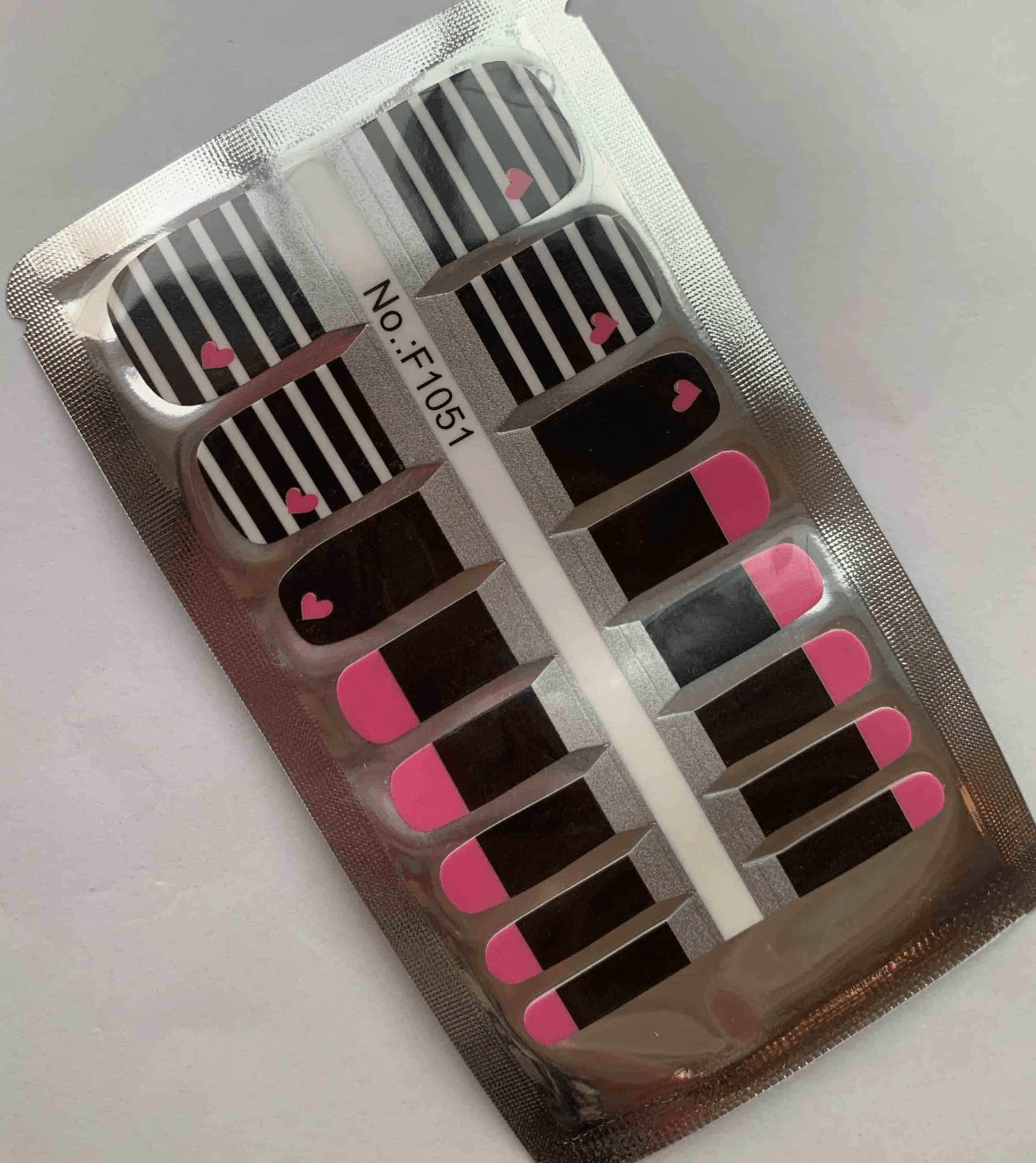 Black and white striped nail wraps with pink hearts in packaging for pedicures