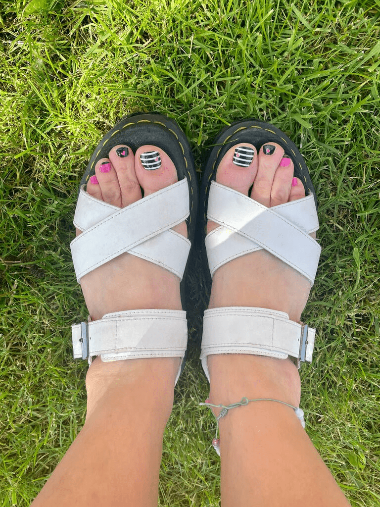 Summer pedicure featuring black striped nail wraps with pink heart accents on feet