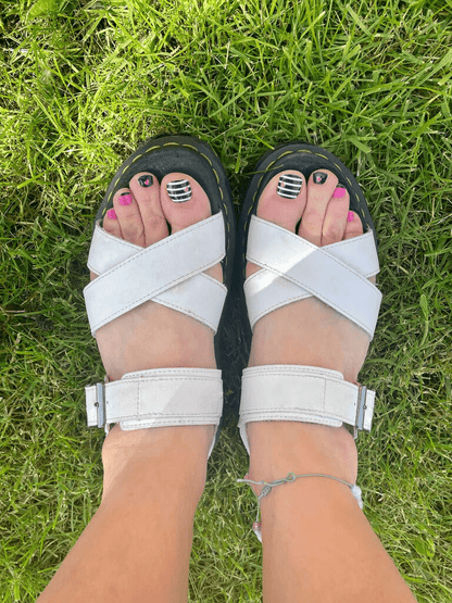 Summer pedicure featuring black striped nail wraps with pink heart accents on feet